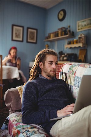 dreads white men - Hipster man using laptop while sitting on sofa with woman in background at home Stock Photo - Premium Royalty-Free, Code: 6109-08705118