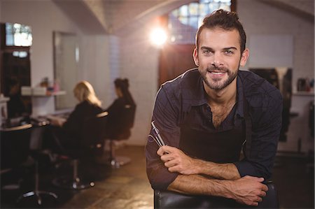 Portrait of smiling male hairdresser leaning on chair in salon Stock Photo - Premium Royalty-Free, Code: 6109-08705291