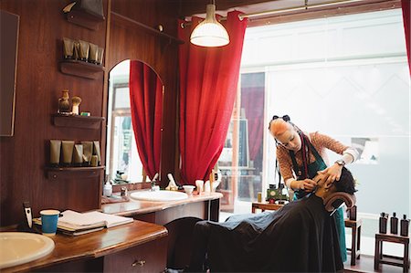 female hair stylist with apron - Man getting his beard shaved in a barber shop Stock Photo - Premium Royalty-Free, Code: 6109-08705351