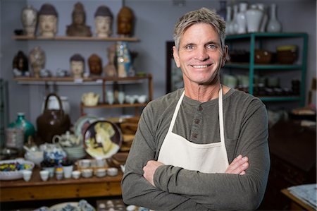 simsearch:6109-08705486,k - Happy male potter standing with arms crossed in pottery workshop Photographie de stock - Premium Libres de Droits, Code: 6109-08705491