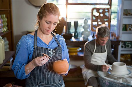 simsearch:6109-08705484,k - Female potter checking pot in pottery workshop Photographie de stock - Premium Libres de Droits, Code: 6109-08705495