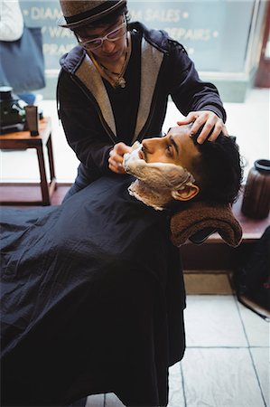 female hair stylist with apron - Man getting his beard shaved with shaving brush in barber shop Foto de stock - Sin royalties Premium, Código: 6109-08705404