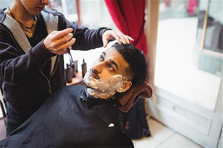 female hair stylist with apron - Man getting his beard shaved with razor in barber shop Foto de stock - Sin royalties Premium, Código: 6109-08705408