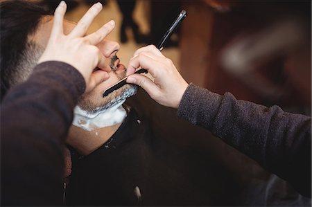 simsearch:6109-08705418,k - Man getting his beard shaved with razor in barber shop Foto de stock - Sin royalties Premium, Código: 6109-08705411