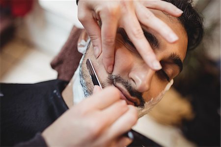 simsearch:6109-08705418,k - Man getting his beard shaved with razor in barber shop Foto de stock - Sin royalties Premium, Código: 6109-08705412