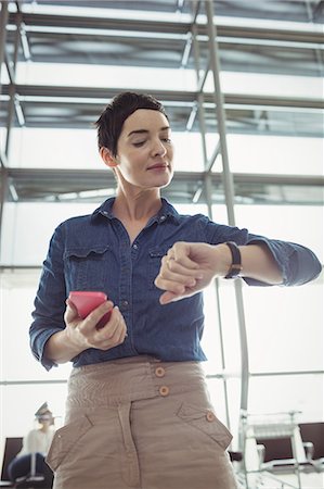 simsearch:6109-08802694,k - Businesswoman checking time while using mobile phone in airport terminal Stock Photo - Premium Royalty-Free, Code: 6109-08722579