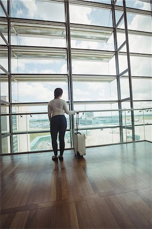 simsearch:6109-08700478,k - Rear view of businesswoman with luggage looking through glass window at airport Foto de stock - Royalty Free Premium, Número: 6109-08722632