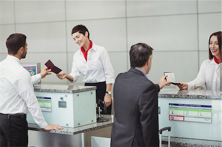 simsearch:6109-08929425,k - Airline check-in attendant handing passport to passenger at airport check-in counter Foto de stock - Sin royalties Premium, Código: 6109-08722704