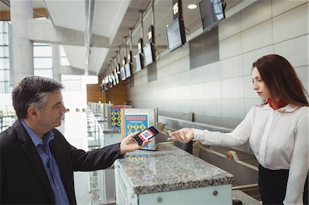 simsearch:6109-08802694,k - Businessman showing mobile boarding pass to airline check-in attendant at check-in counter Stock Photo - Premium Royalty-Free, Code: 6109-08722735