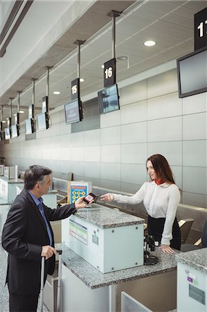 simsearch:6109-08802694,k - Businessman showing mobile boarding pass to airline check-in attendant at check-in counter Stock Photo - Premium Royalty-Free, Code: 6109-08722736