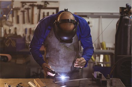 simsearch:6109-08722790,k - Male welder working on a piece of metal in workshop Foto de stock - Sin royalties Premium, Código: 6109-08722801
