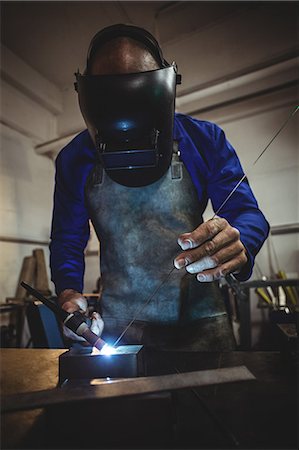 simsearch:6109-08722814,k - Male welder working on a piece of metal in workshop Foto de stock - Royalty Free Premium, Número: 6109-08722802