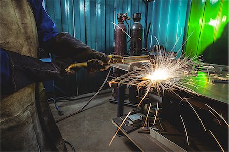 simsearch:6109-08722895,k - Mid-section of female welder working on a piece of metal in workshop Foto de stock - Sin royalties Premium, Código: 6109-08722901