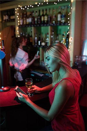 simsearch:400-04281366,k - Woman using mobile phone while having a glass of wine at counter in bar Photographie de stock - Premium Libres de Droits, Code: 6109-08801990