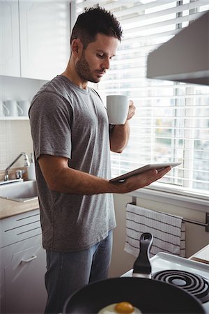 simsearch:6113-07790487,k - Man using digital tablet while having coffee in kitchen at home Photographie de stock - Premium Libres de Droits, Code: 6109-08802245