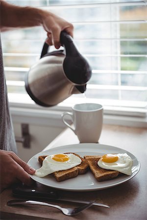 Man holding his breakfast plate while pouring hot water into mug in the kitchen Stock Photo - Premium Royalty-Free, Code: 6109-08802248