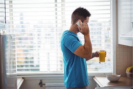 simsearch:6109-08802258,k - Man talking on mobile phone while using having glass of juice in kitchen at home Photographie de stock - Premium Libres de Droits, Code: 6109-08802253