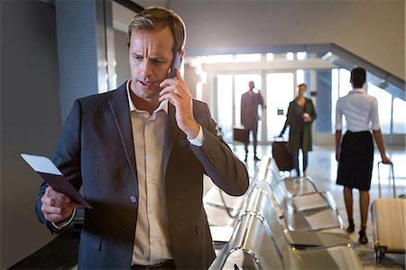 simsearch:6109-08802775,k - Businessman talking on his phone while holding passport and hoarding pass at airport terminal Photographie de stock - Premium Libres de Droits, Code: 6109-08802771