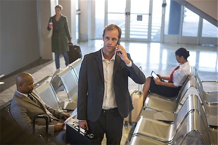 Businessman with briefcase talking on his phone while standing at airport terminal Stock Photo - Premium Royalty-Free, Code: 6109-08802774