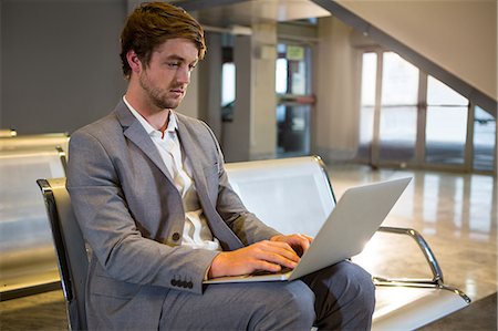 simsearch:6109-08929459,k - Businessman working on his laptop in the waiting area at the airport terminal Foto de stock - Royalty Free Premium, Número: 6109-08802710