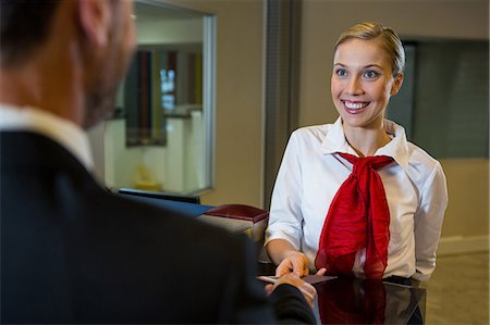 Female staff giving boarding pass to the businessman at the check in desk Foto de stock - Sin royalties Premium, Código: 6109-08802726