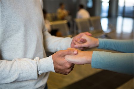 Mid-section of couple holding hands in waiting area at airport terminal Stock Photo - Premium Royalty-Free, Code: 6109-08802813