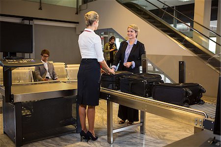 simsearch:6109-08929511,k - Businesswoman interacting with airport staff with luggage kept on conveyor belt at airport terminal Foto de stock - Sin royalties Premium, Código: 6109-08802831
