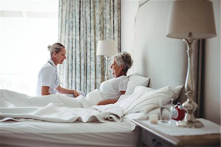 Nurse interacting with senior woman on bed at bedroom Foto de stock - Sin royalties Premium, Código: 6109-08803157