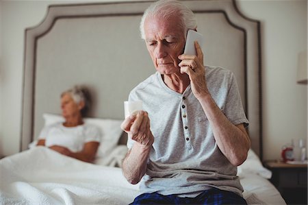 Worried senior man sitting in bedroom holding medicine and talking on mobile phone Photographie de stock - Premium Libres de Droits, Code: 6109-08803167