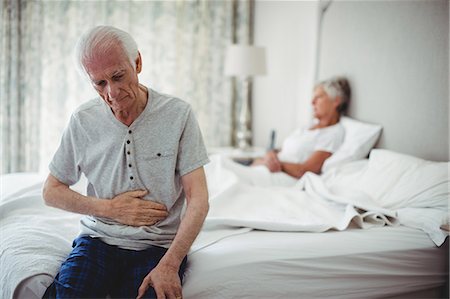 senior stress home - Worried senior man with hand on stomach sitting in bedroom Stock Photo - Premium Royalty-Free, Code: 6109-08803168