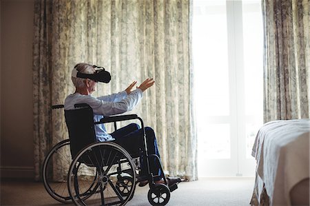 Senior man sitting on wheelchair and using virtual reality headset in bedroom at home Stock Photo - Premium Royalty-Free, Code: 6109-08803128