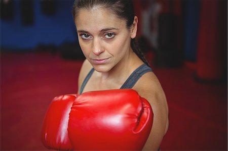 simsearch:6109-08803789,k - Portrait of confident female boxer performing boxing stance in fitness studio Photographie de stock - Premium Libres de Droits, Code: 6109-08803751