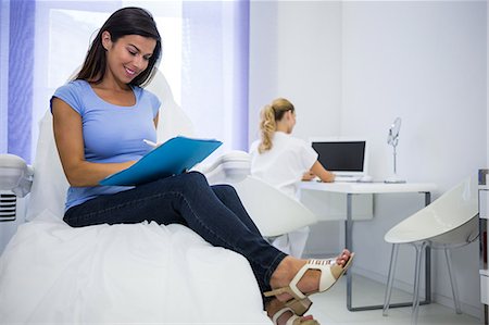simsearch:6109-08804160,k - Female patient sitting and writing on clipboard at clinic Foto de stock - Sin royalties Premium, Código: 6109-08804096