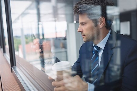 simsearch:6109-08830034,k - Businessman using mobile phone and holding disposable coffee cup in office Fotografie stock - Premium Royalty-Free, Codice: 6109-08804204