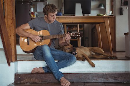 people sitting playing a guitar - Man playing guitar at home, dog lying beside him Stock Photo - Premium Royalty-Free, Code: 6109-08804481