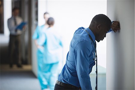 simsearch:6109-08689539,k - Sad doctor leaning on wall in hospital corridor Stock Photo - Premium Royalty-Free, Code: 6109-08804417