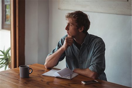 simsearch:6109-08944685,k - Thoughtful man sitting desk with notebook and coffee cup at home Stock Photo - Premium Royalty-Free, Code: 6109-08804564