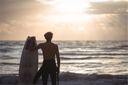 simsearch:649-07437735,k - Rear view of a man carrying surfboard standing on beach at dusk Photographie de stock - Premium Libres de Droits, Code: 6109-08804530