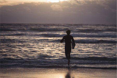 simsearch:400-07952891,k - Silhouette of a man carrying surfboard running towards sea at dusk Stock Photo - Premium Royalty-Free, Code: 6109-08804536