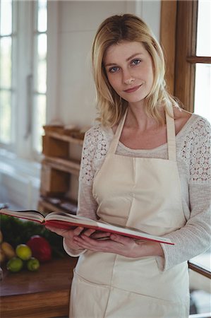 female kitchen aprons - Portrait of beautiful woman holding recipe book in kitchen at home Stock Photo - Premium Royalty-Free, Code: 6109-08804620