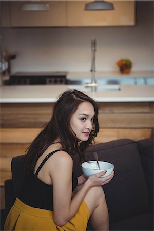 simsearch:6109-08944595,k - Woman sitting on sofa eating breakfast cereal in living room at home Photographie de stock - Premium Libres de Droits, Code: 6109-08804757