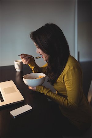simsearch:614-08219959,k - Woman eating cereal while working on laptop in study room at home Foto de stock - Sin royalties Premium, Código: 6109-08804775