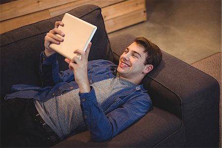 simsearch:6109-08944589,k - Smiling man lying on sofa using digital tablet in living room at home Stock Photo - Premium Royalty-Free, Code: 6109-08804795