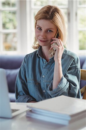 simsearch:6109-08537097,k - Beautiful woman talking on mobile phone while using laptop in living room at home Stock Photo - Premium Royalty-Free, Code: 6109-08804730