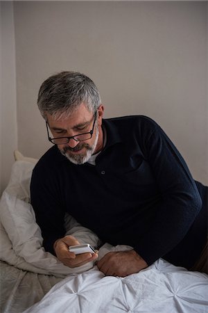 simsearch:6109-08804993,k - Man using mobile phone on bed at home Fotografie stock - Premium Royalty-Free, Codice: 6109-08804882