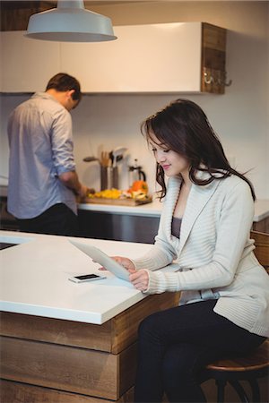 Woman using digital tablet while man working in background at kitchen Stock Photo - Premium Royalty-Free, Code: 6109-08804803