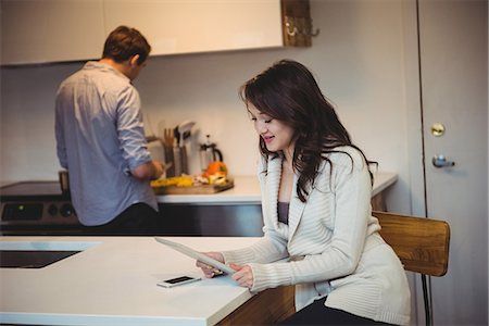 Woman using digital tablet while man working in background at kitchen Stock Photo - Premium Royalty-Free, Code: 6109-08804801