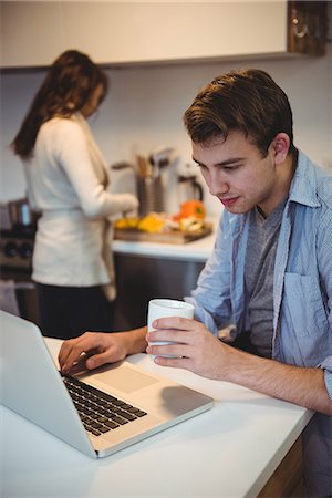 simsearch:6109-06781541,k - Man using laptop while woman working in background at kitchen Stock Photo - Premium Royalty-Free, Code: 6109-08804804