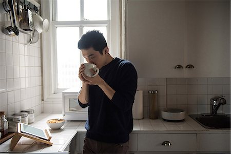 Man using digital tablet while having a cup of coffee at home Stock Photo - Premium Royalty-Free, Code: 6109-08804942