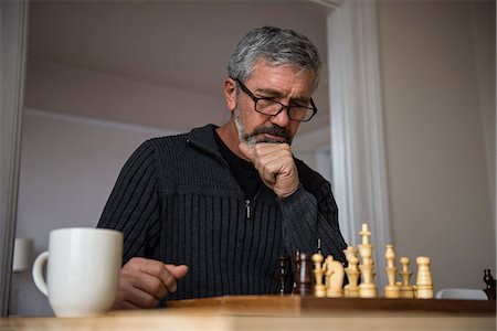 Attentive man playing chess at home Stock Photo - Premium Royalty-Free, Code: 6109-08804946